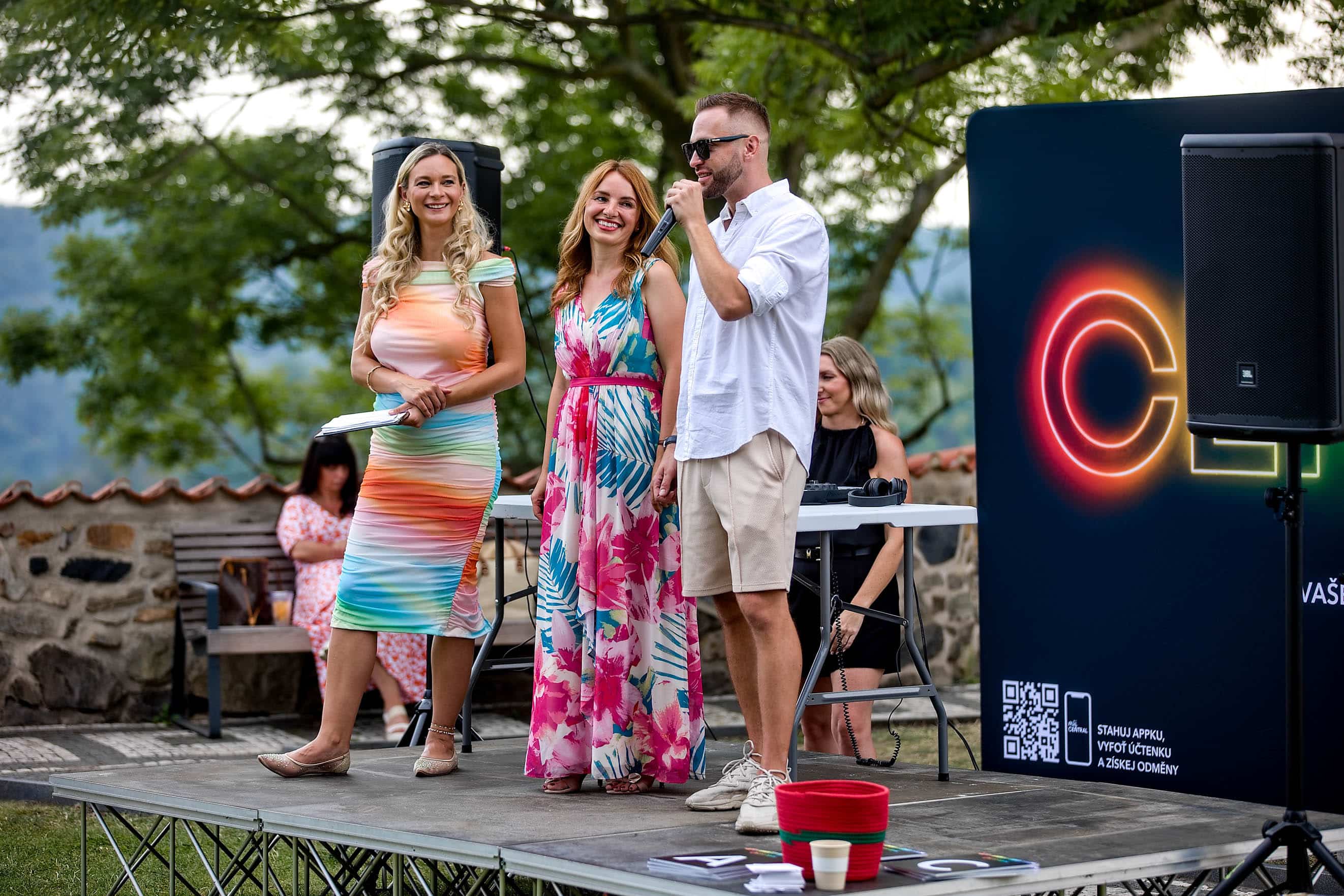 Tři lidé stojí na pódiu venkovní akce